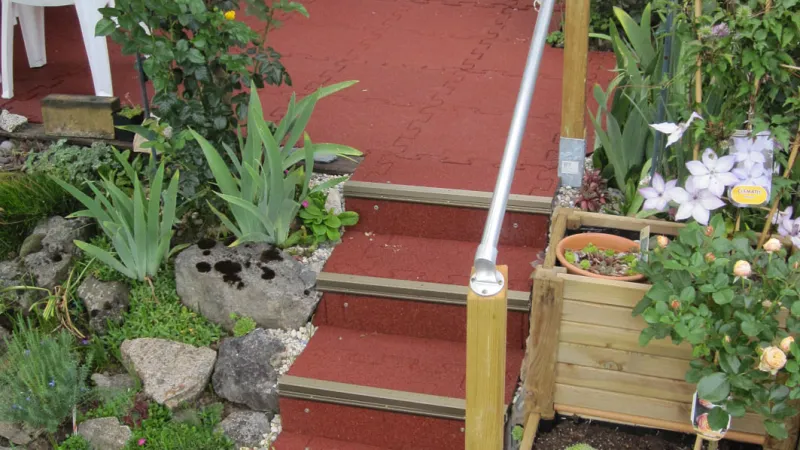 Red staircase leads to the terrace. Green plants grow around the WARCO stair covering.