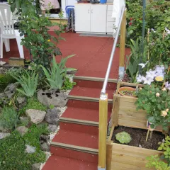 Red staircase leads to the terrace. Green plants grow around the WARCO stair covering.