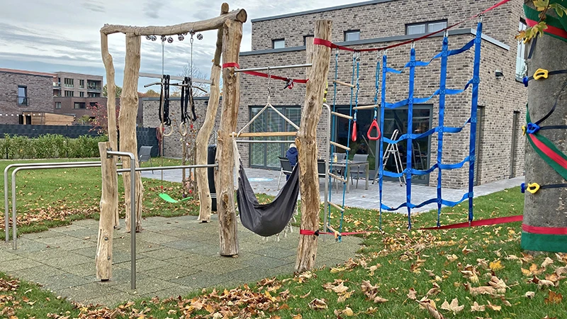 A climbing frame on a tree with nets. Next to it, a few wooden posts with a punching bag, horizontal bar and swing.